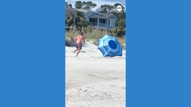 Video Man in patriotic bathing suit chases runaway beach umbrella